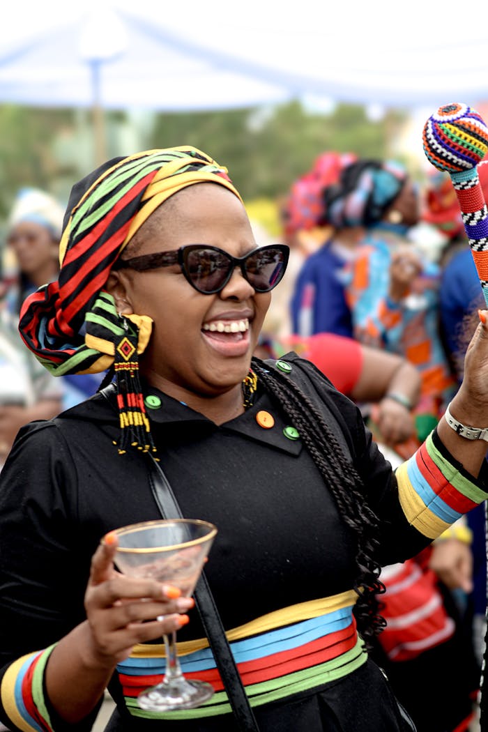 Woman in colorful attire celebrating at an outdoor cultural festival with a vibrant crowd.